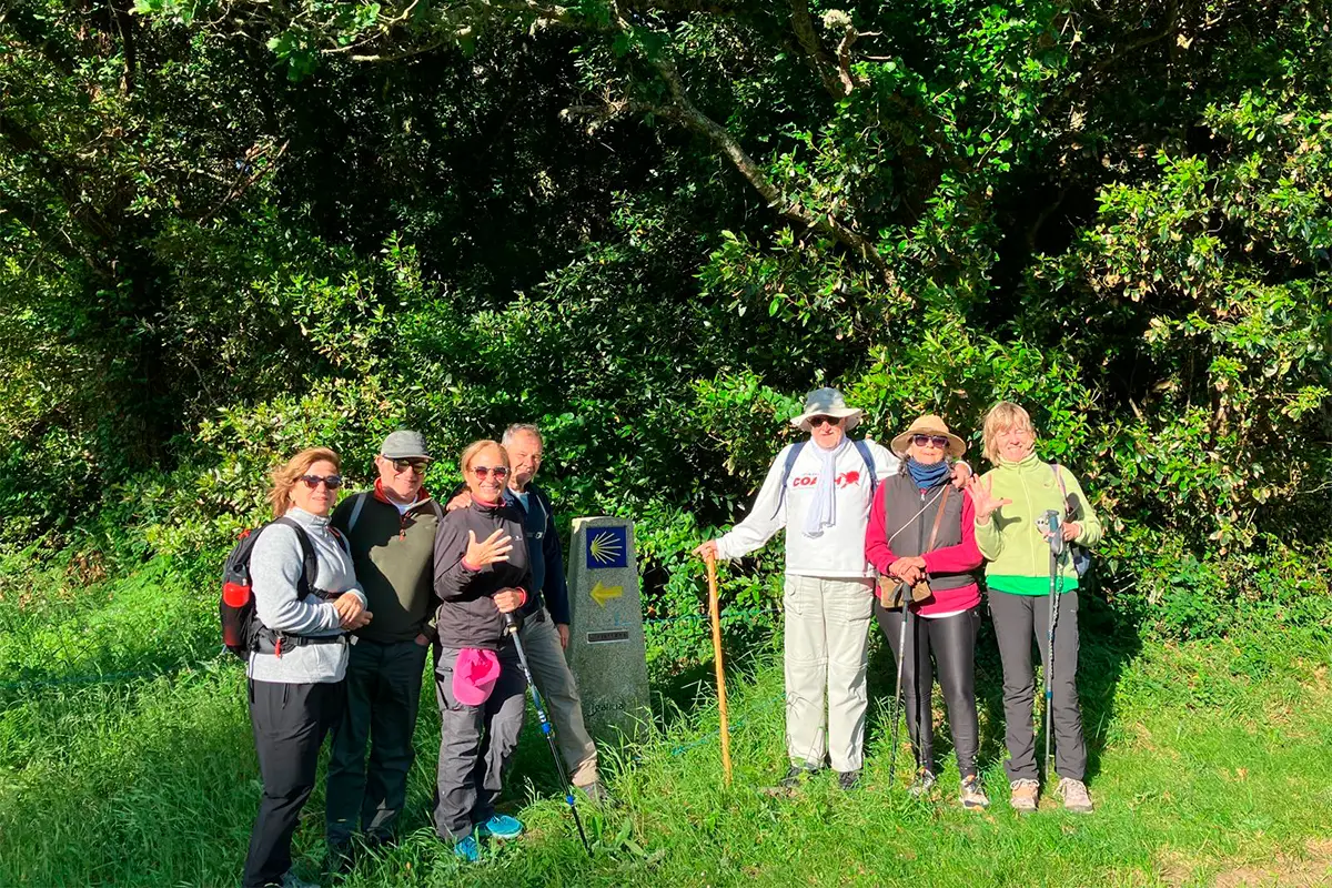 Peregrinos en medio de la naturaleza junto a un mojón del Camino de Finisterre